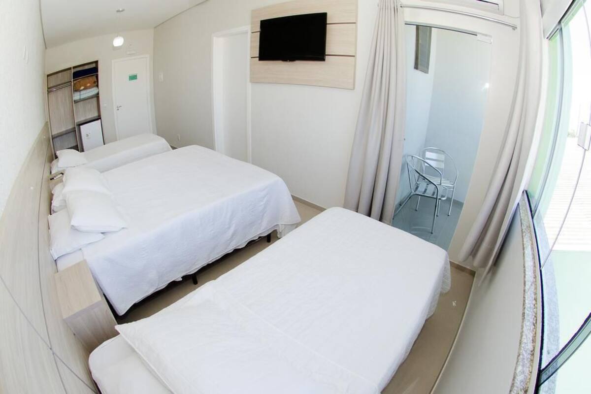 A hotel room with two beds, a TV mounted on the wall, and a small seating area with a chair and table.