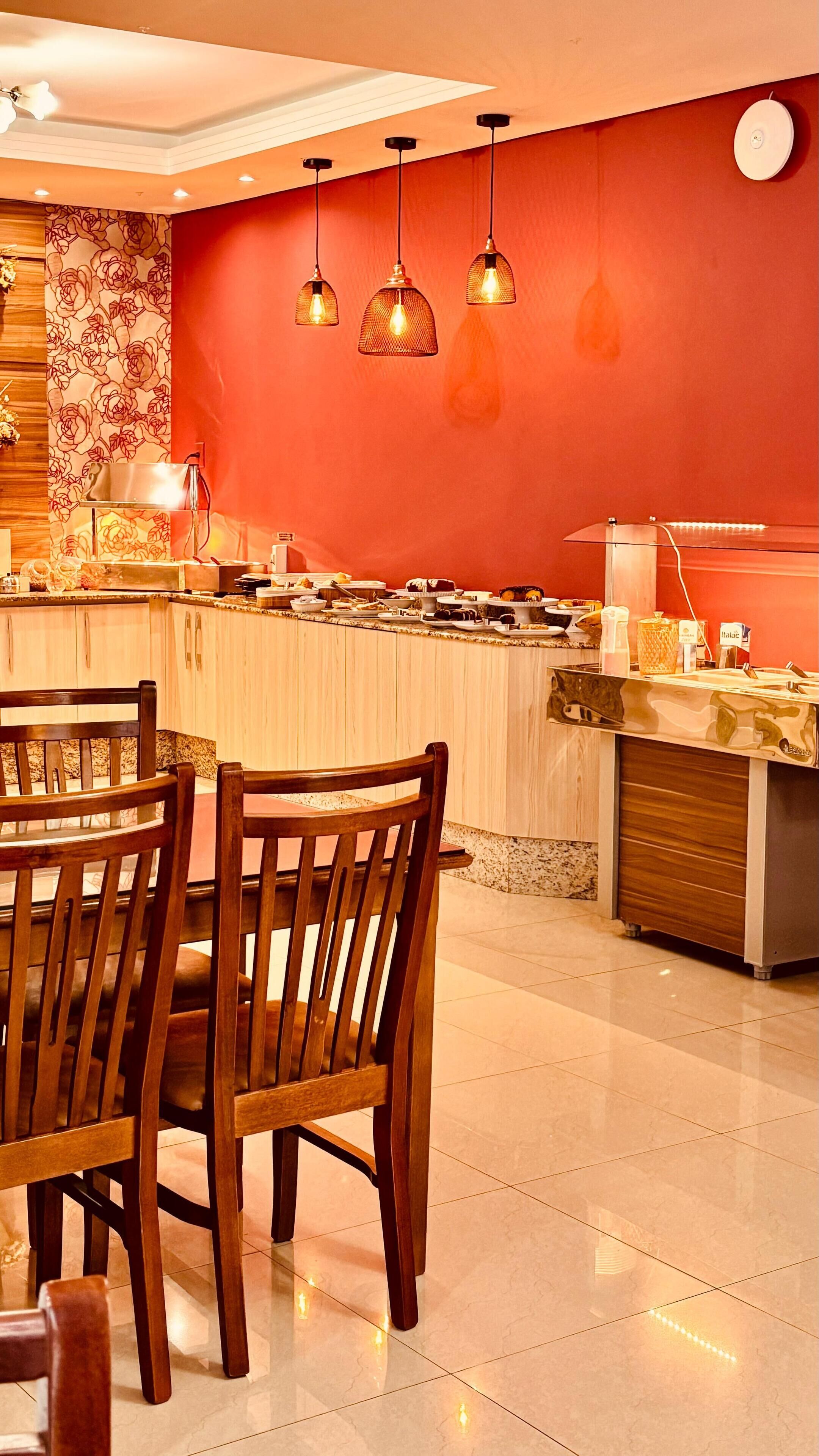 A restaurant with a red wall, wooden chairs, and hanging pendant lights.