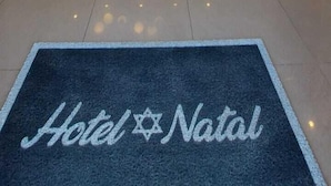 A hotel reception area with a chandelier, a reception desk, a doormat, and a wall with a framed picture. - Hotel Natal (Penha)