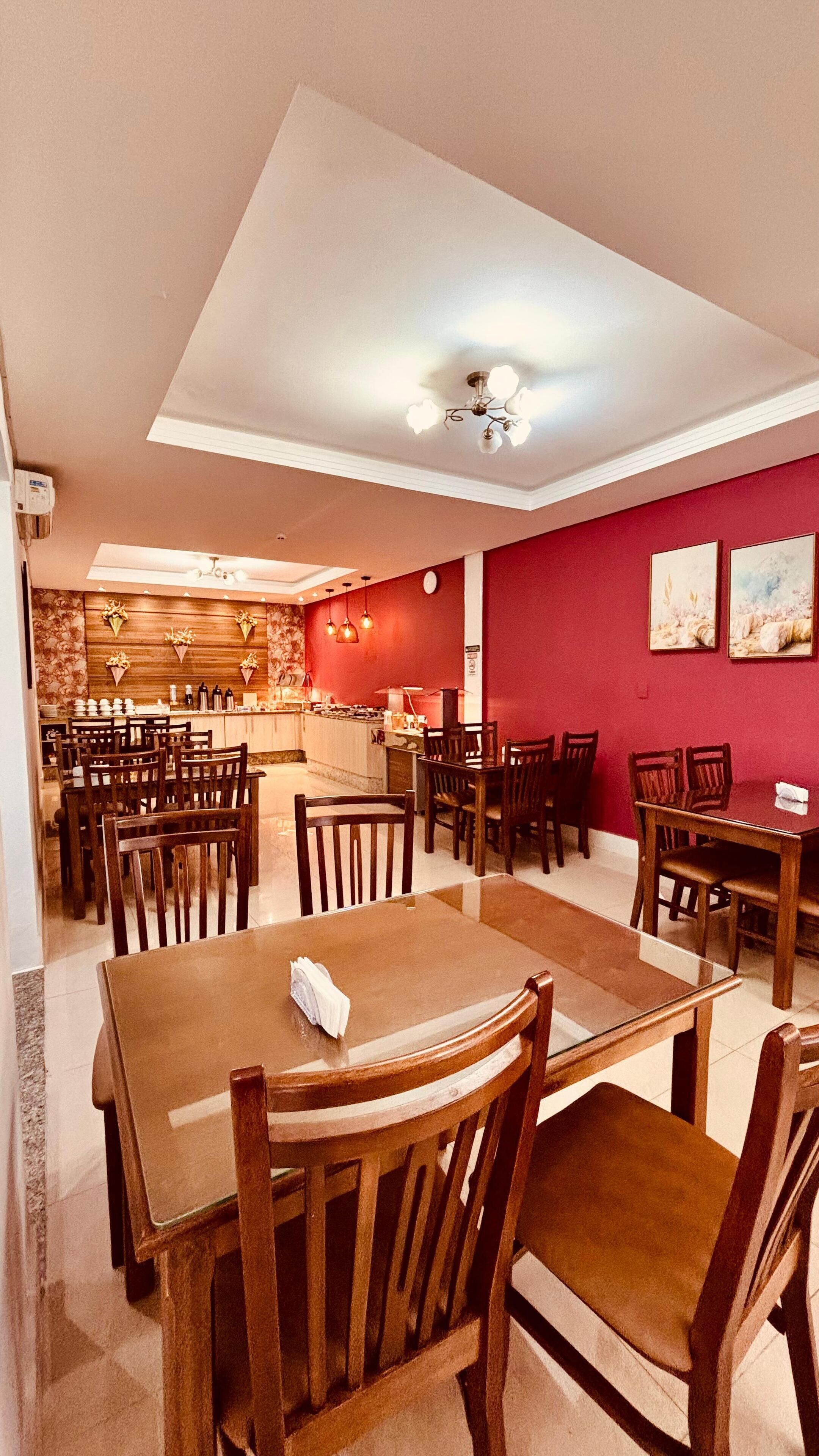 A restaurant with multiple wooden tables and chairs, a kitchen area, and red walls with artwork.