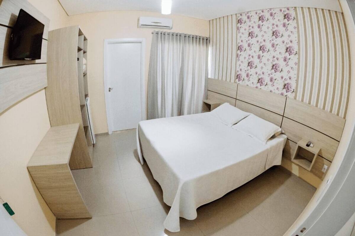 A bedroom with a bed, a TV mounted on the wall, a wardrobe, and a door.