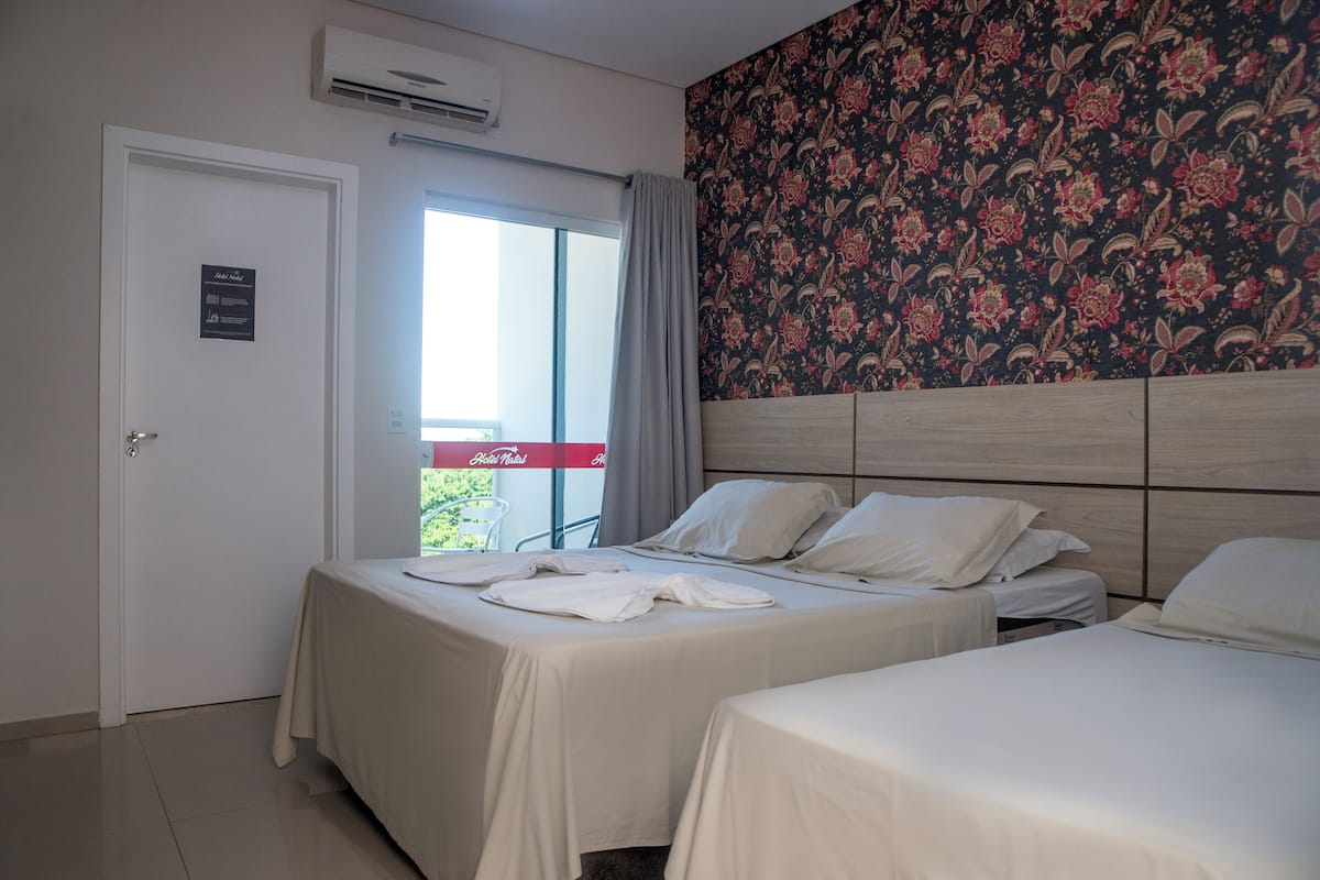 A hotel room with two beds, a balcony with a red sign, and a floral wallpaper.