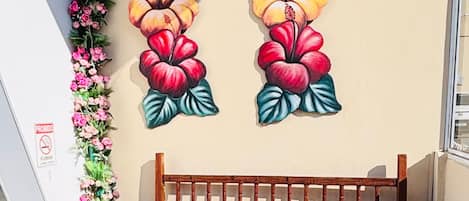 Un banc en bois agrémenté d’un coussin à motifs floraux, placé contre un mur orné d’une fresque florale et surmonté d’un jardin vertical.