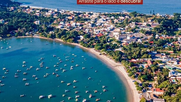 An aerial view of a coastal town with a marina filled with boats, a pier, and a mix of residential and commercial buildings. - Hotel Natal (Penha)