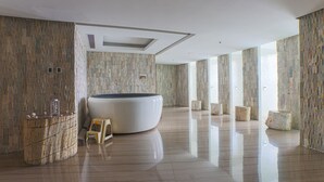 Ein geräumiger Raum mit einer großen, gewölbten Badewanne, einem kleinen Hocker und einer Holzeinrichtung mit Dekorationselementen.