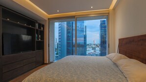 Ein Schlafzimmer mit einem großen Bett, einem Fernseher und Blick auf die Stadt durch eine Glastür.