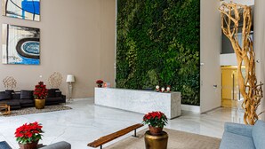 Ein modernes Wohnzimmer mit einem grauen Sofa, einer Holzbank und einem Empfangstresen an einer grünen Wand.
