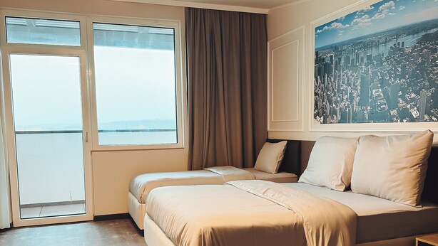 A modern bedroom with a large bed, a cityscape view, and a large window. - F Hotel 24h Check-In (Hoersching)