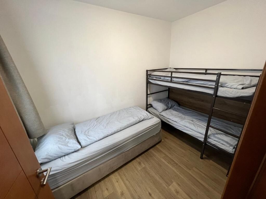 Ein kleines Zimmer mit einem Einzelbett, Holzboden und einer Tür.