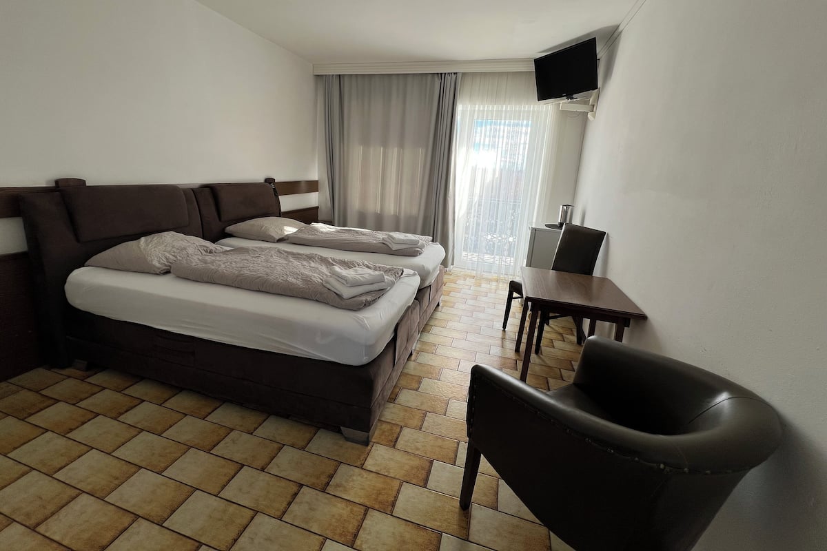 A hotel room with two beds, a desk, a chair, a television, and a window with curtains.