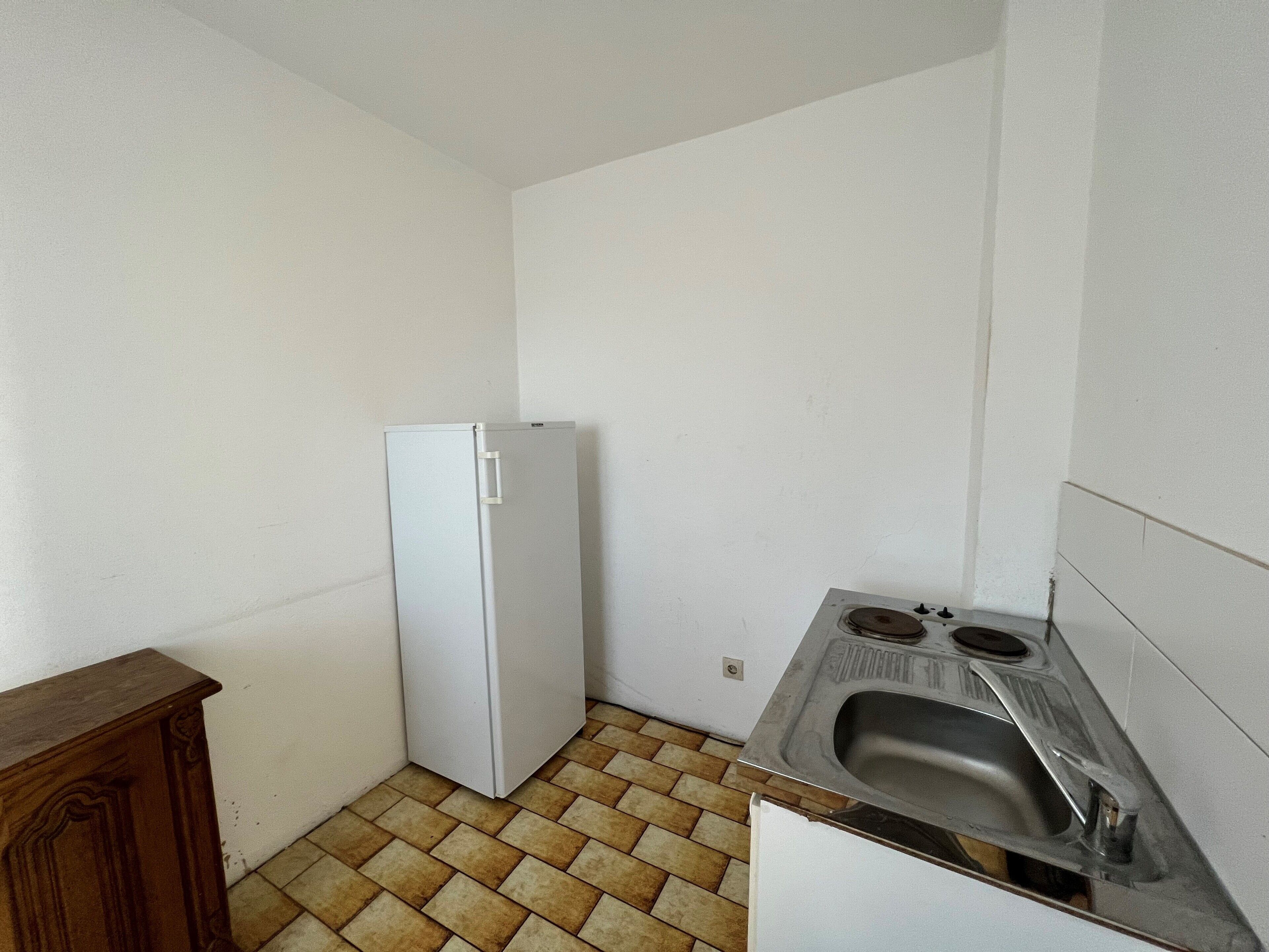 A small kitchen with a white refrigerator, a wooden cabinet, and a sink with a metal basin.
