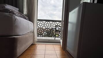 A small, compact room with a sofa, a refrigerator, and a view of the sky through a balcony door.