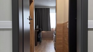 A hallway leading to a room with a bed, a small table, and a chair. - F Hotel 24h Check-In (Hoersching)