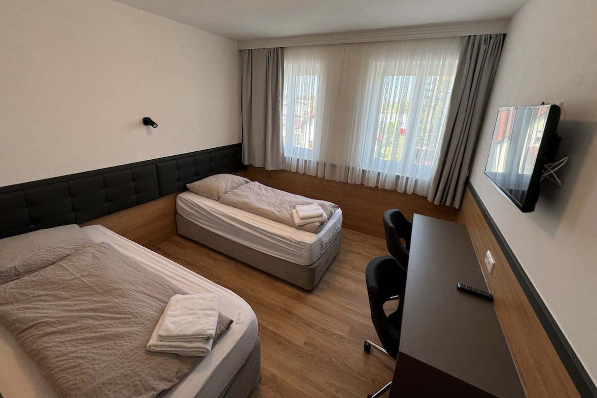 A hotel room with two beds, a desk, a chair, and a TV mounted on the wall.