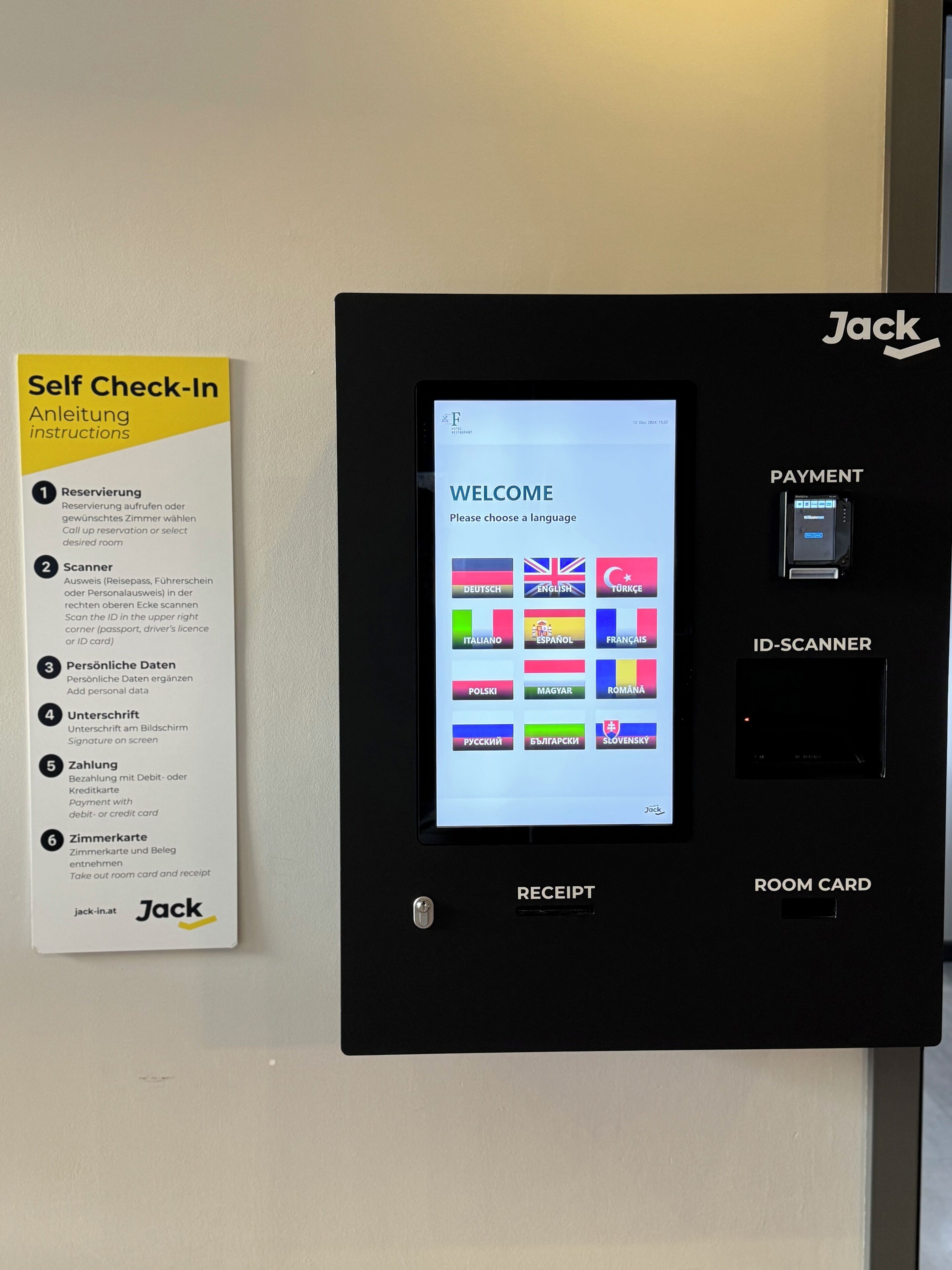 En självbetjäningskiosk med en pekskärm, en betalterminal och en kortläsare för rumskort. Instruktioner finns på en skylt i närheten.