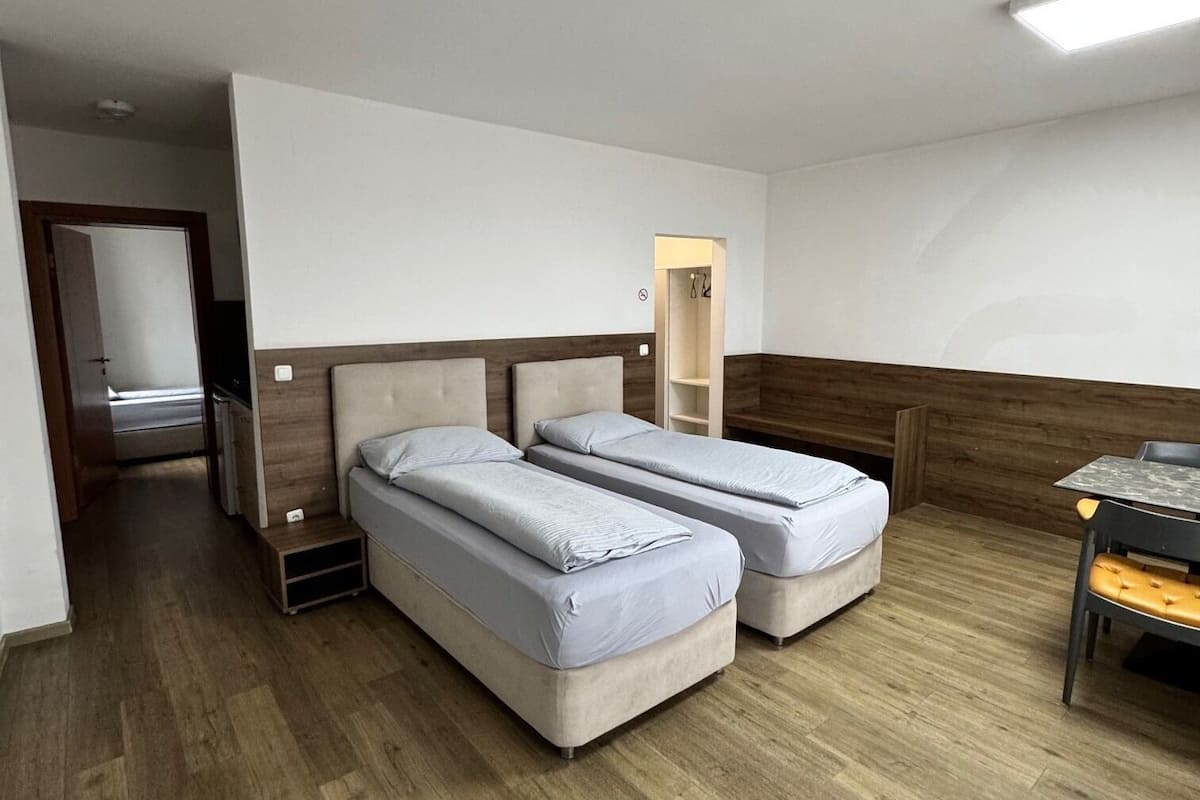 A hotel room with two beds, a wooden floor, a desk with a chair, and a mirror.