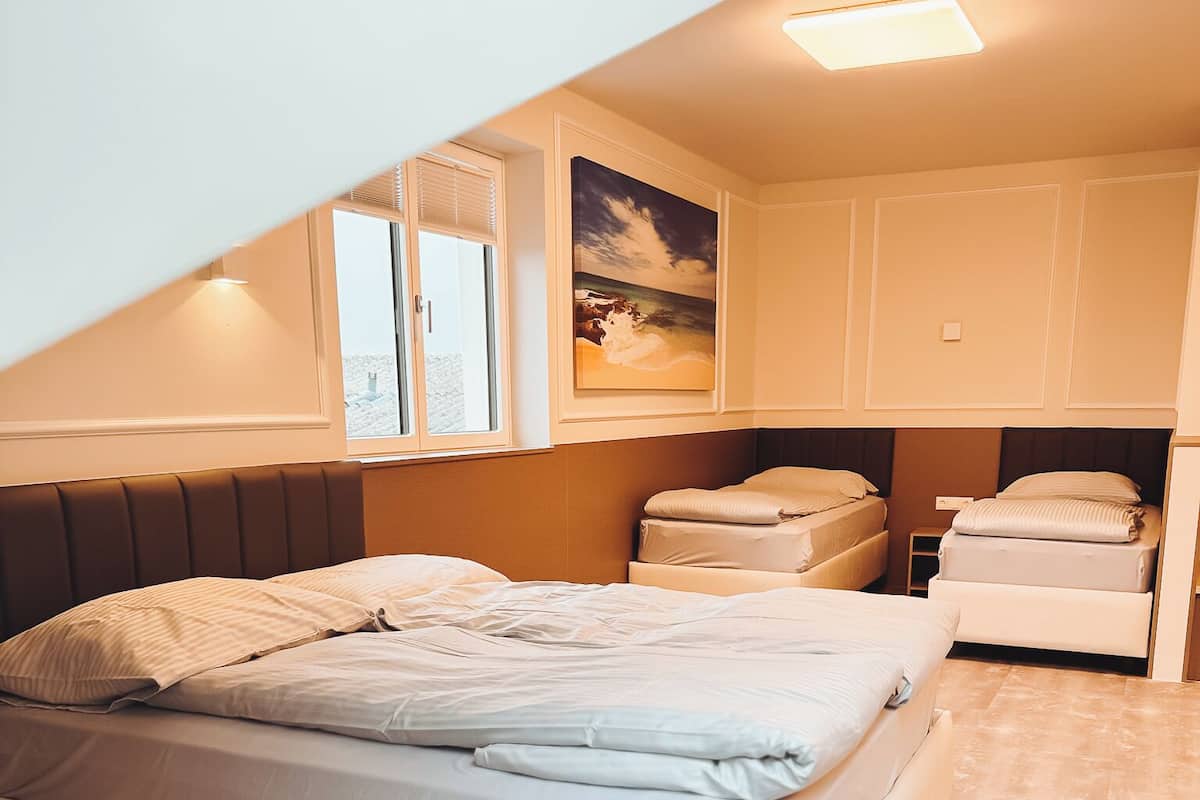 A bedroom with a large bed, a small bedside table, and a window with blinds.