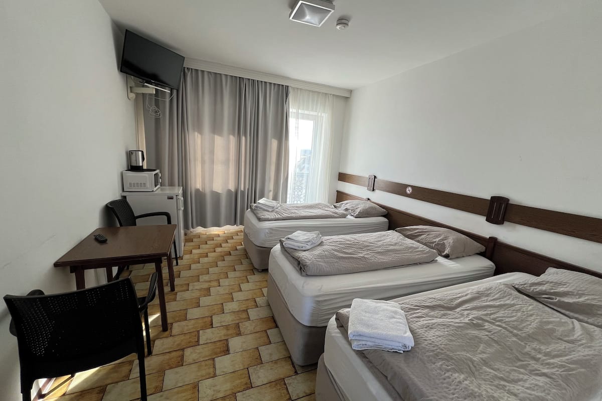 A hotel room with two beds, a desk, a chair, a TV, and a window with curtains.