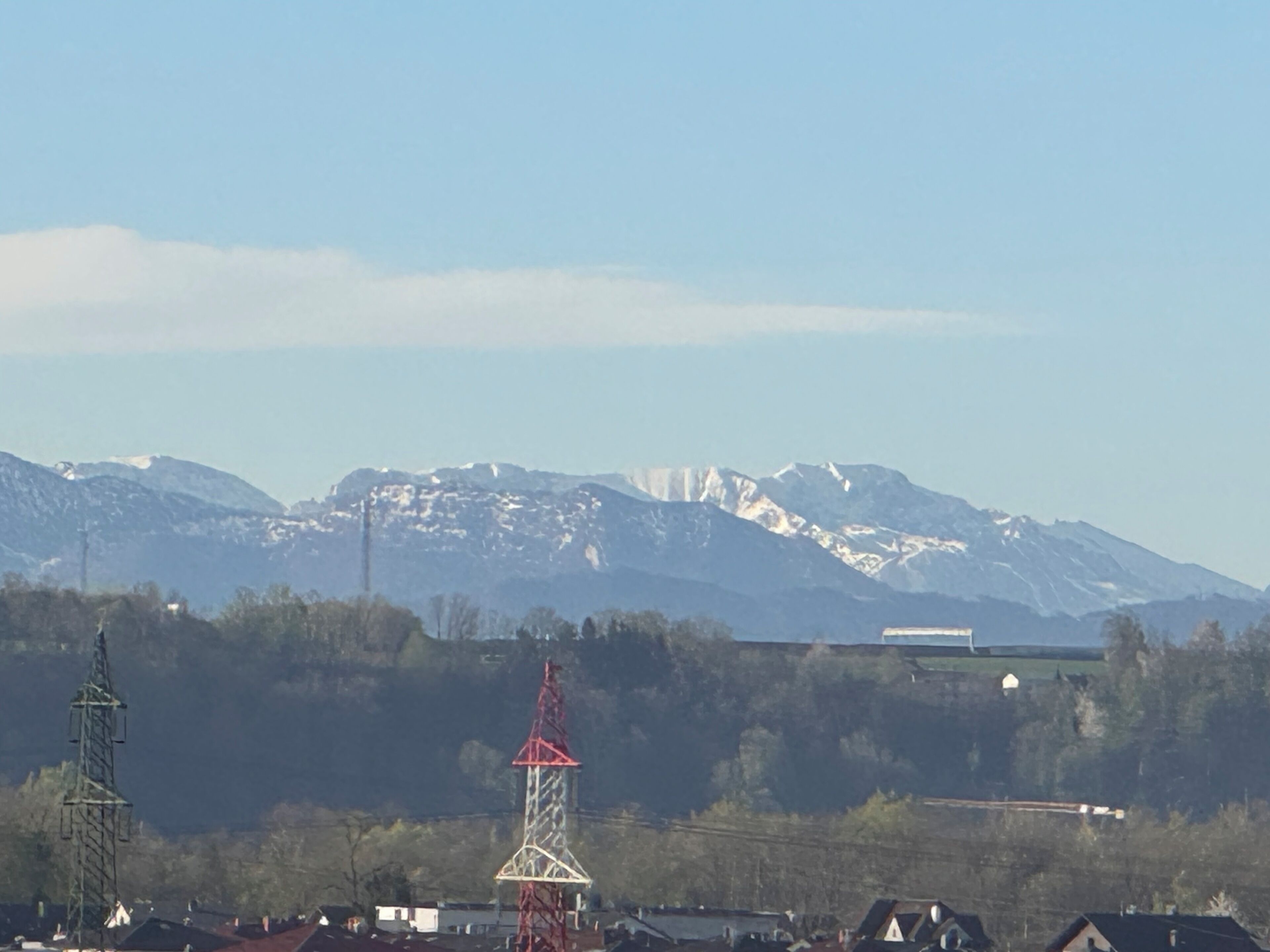 A mountain range with snow-capped peaks, a red and white tower, and residential buildings in the foreground.