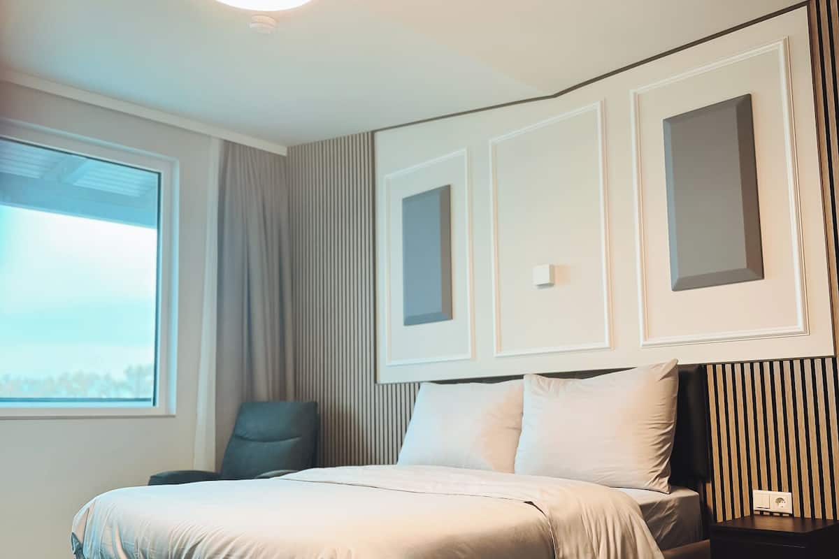 A modern hotel room with a large bed, a bedside table, a nightstand, and a window with curtains.