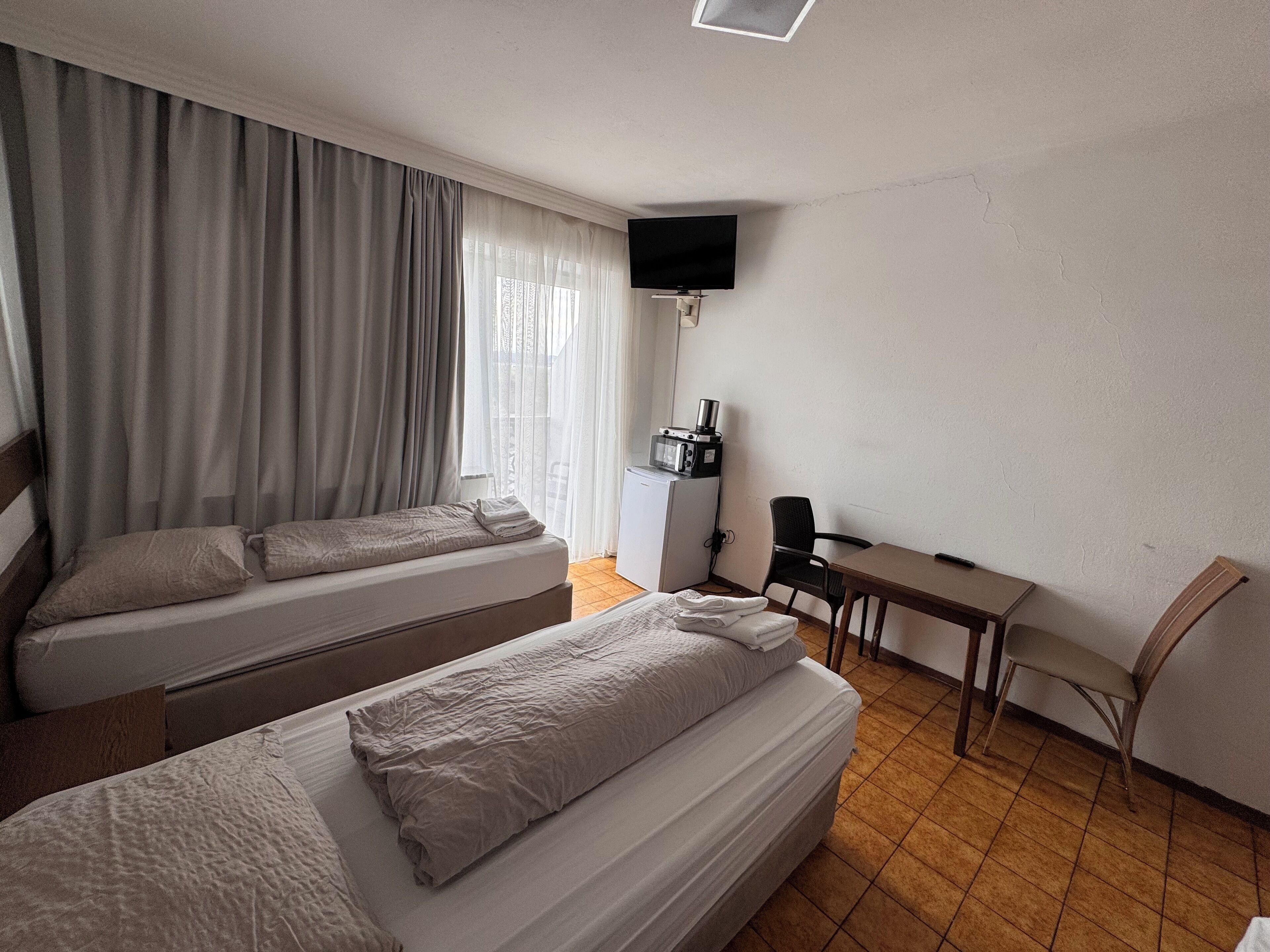 Ein Hotelzimmer mit zwei Betten, einem Schreibtisch, einem Stuhl, einem Fernseher und einer Küchenzeile.