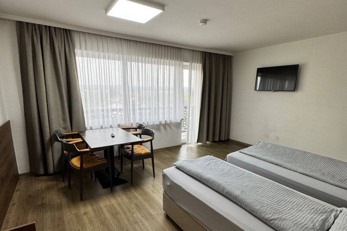 A room with a bed, a table with chairs, a TV, and a window with curtains.