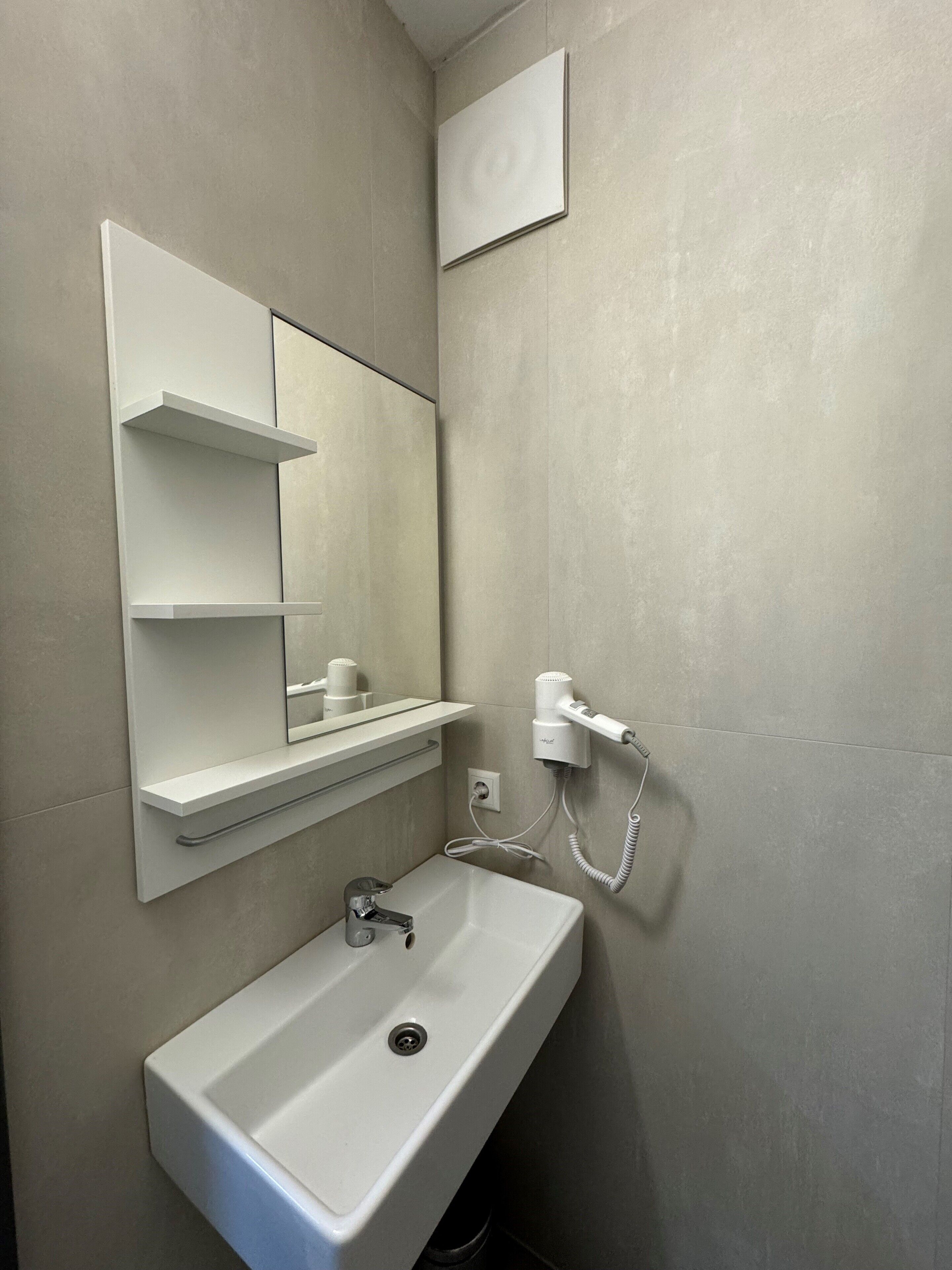A bathroom with a white sink, a mirror, and a hairdryer mounted on the wall.