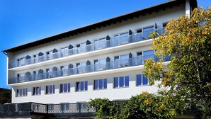 A multi-story hotel with balconies on each floor, a flat roof, and a clear blue sky. - F Hotel 24h Check-In (Hoersching)