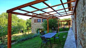 Un patio couvert avec un bâtiment en pierre, une table avec des chaises et une pelouse.