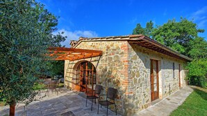 A stone building with a wooden door and arched window, outdoor seating, and a pergola. - Mulignone 1 - Apartment with pool (Molino D'elsa)