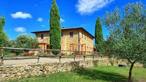 A stone building with a wooden pergola in front, surrounded by greenery and a clear blue sky.