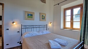 A bedroom with a bed, two wall-mounted light fixtures, a window with curtains, and two framed pictures on the wall.