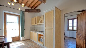 A kitchen with wooden cabinets, a stove, and a refrigerator. There is a window with curtains and a door leading to another room.