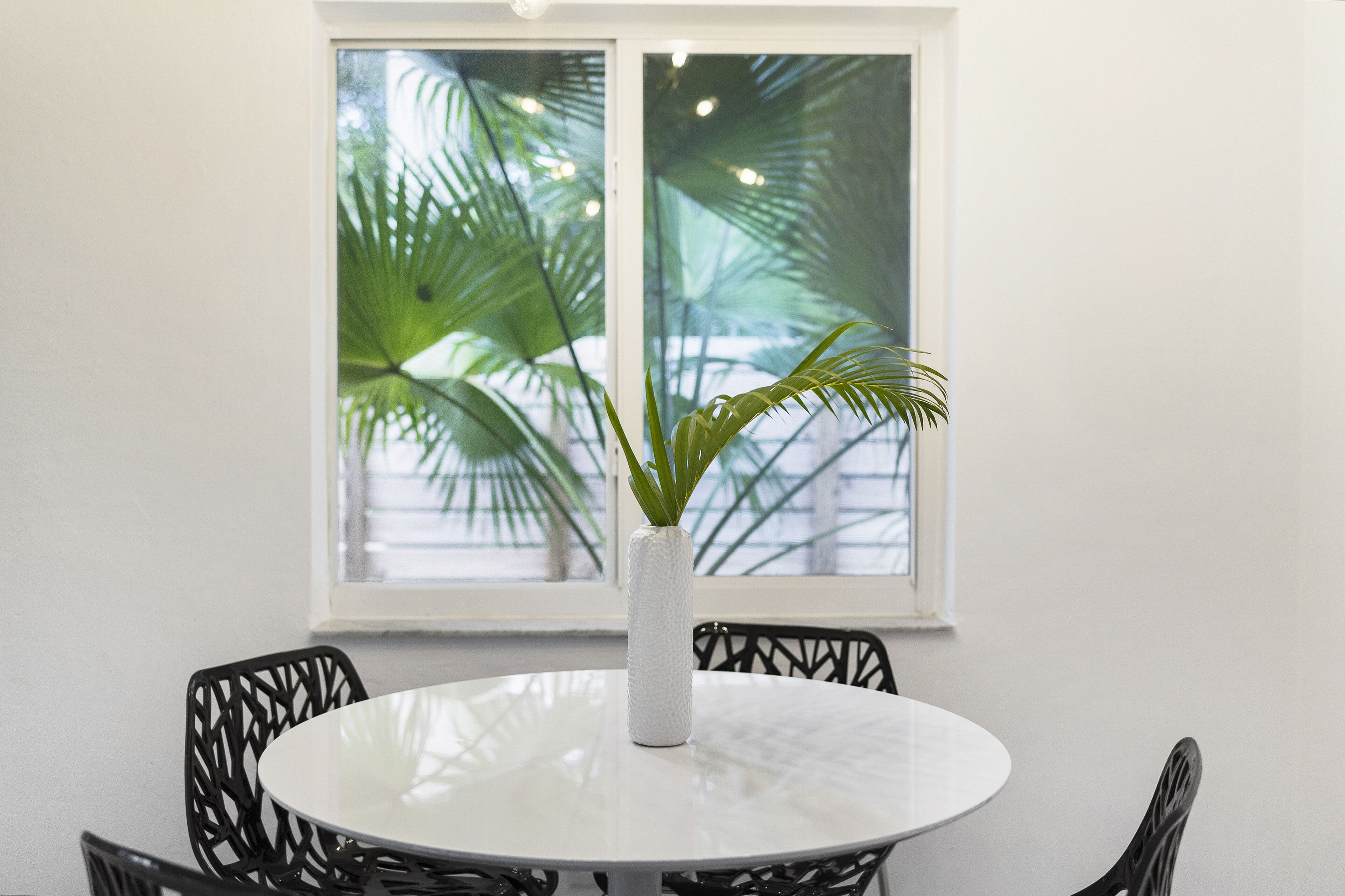 A round white table with a textured white vase in the center, surrounded by black chairs.