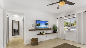 A modern living room with a television, ceiling fan, and large windows.