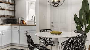 A modern kitchen with white cabinets, a round dining table, black chairs, and a hanging light fixture.