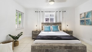 A bedroom with a wooden headboard, a large bed, two bedside tables with lamps, a ceiling fan, and a window with curtains.