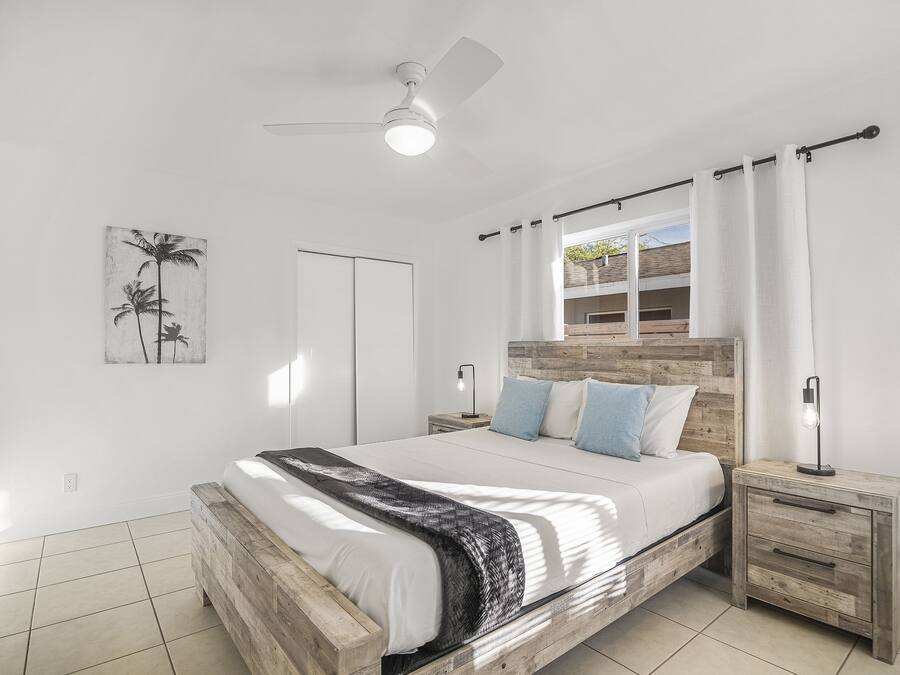 Ein Schlafzimmer mit Holzbett, weißer Bettwäsche, Deckenventilator und Nachttisch mit Lampe.