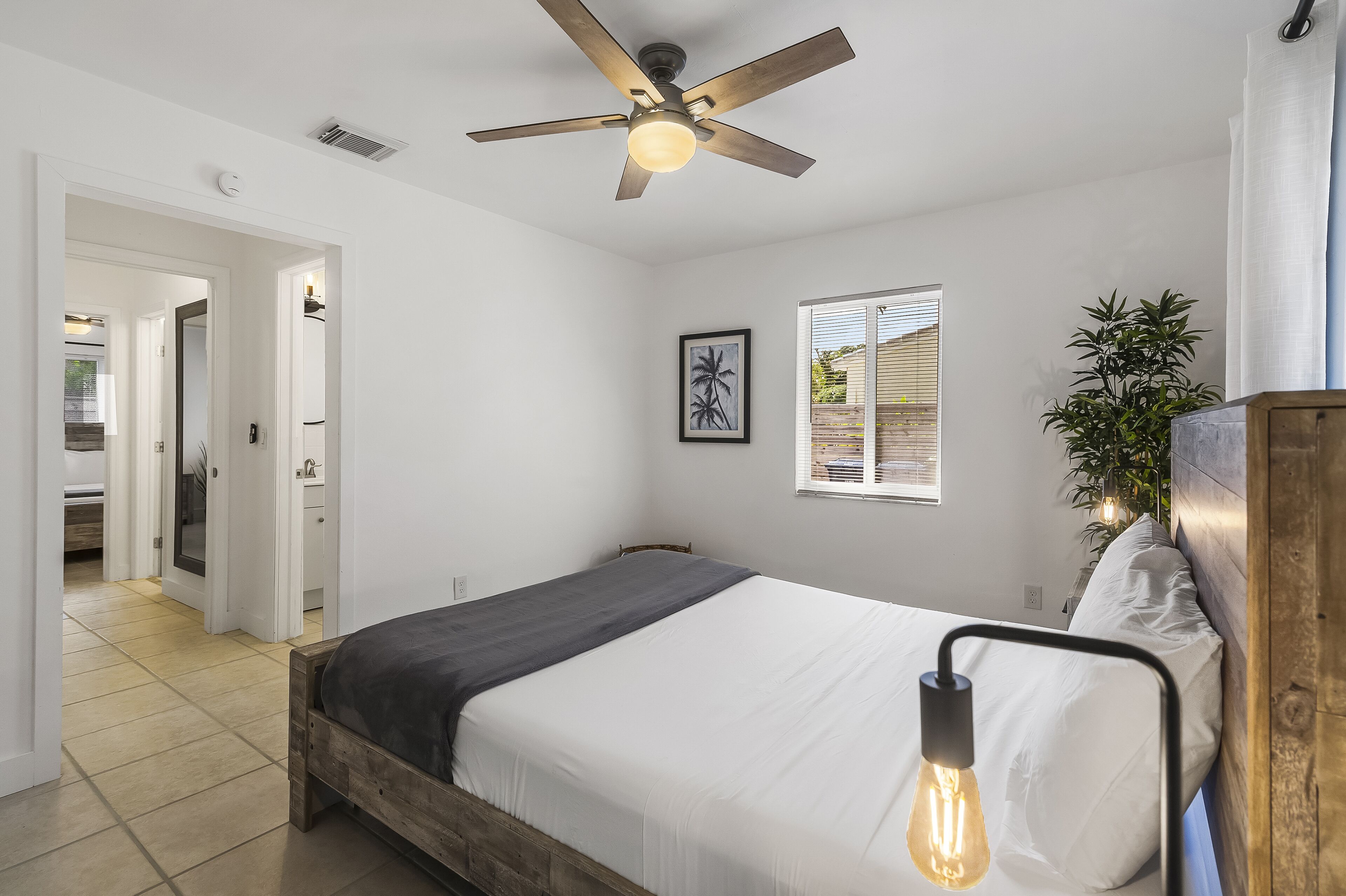 Une chambre à coucher avec un lit, un ventilateur de plafond, une fenêtre et une plante.