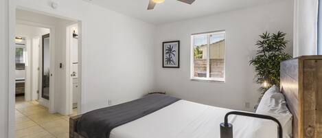 Une chambre à coucher avec un lit, un ventilateur de plafond, une fenêtre et une plante.