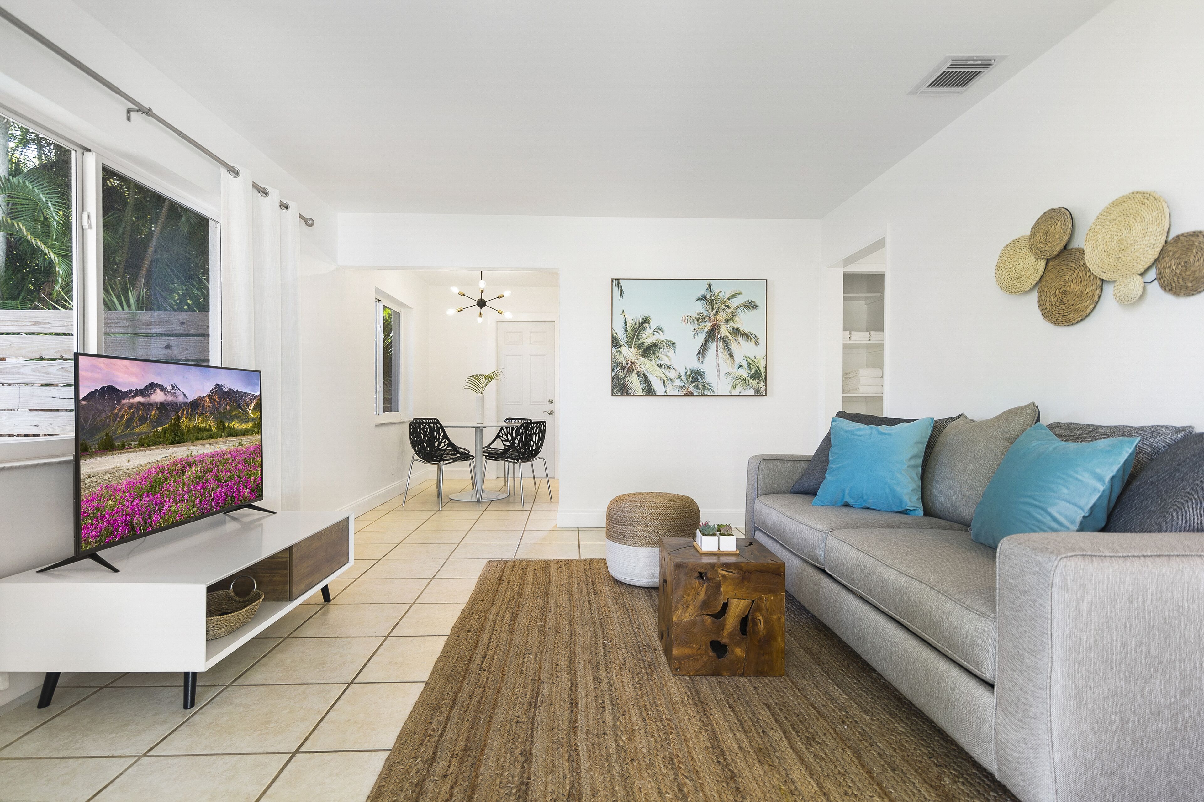A modern living room with a flat-screen TV, grey sofa, and a dining area with chairs.