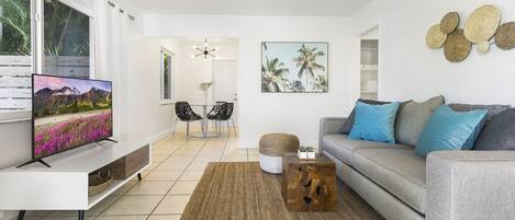A modern living room with a flat-screen TV, grey sofa, and a dining area with chairs.