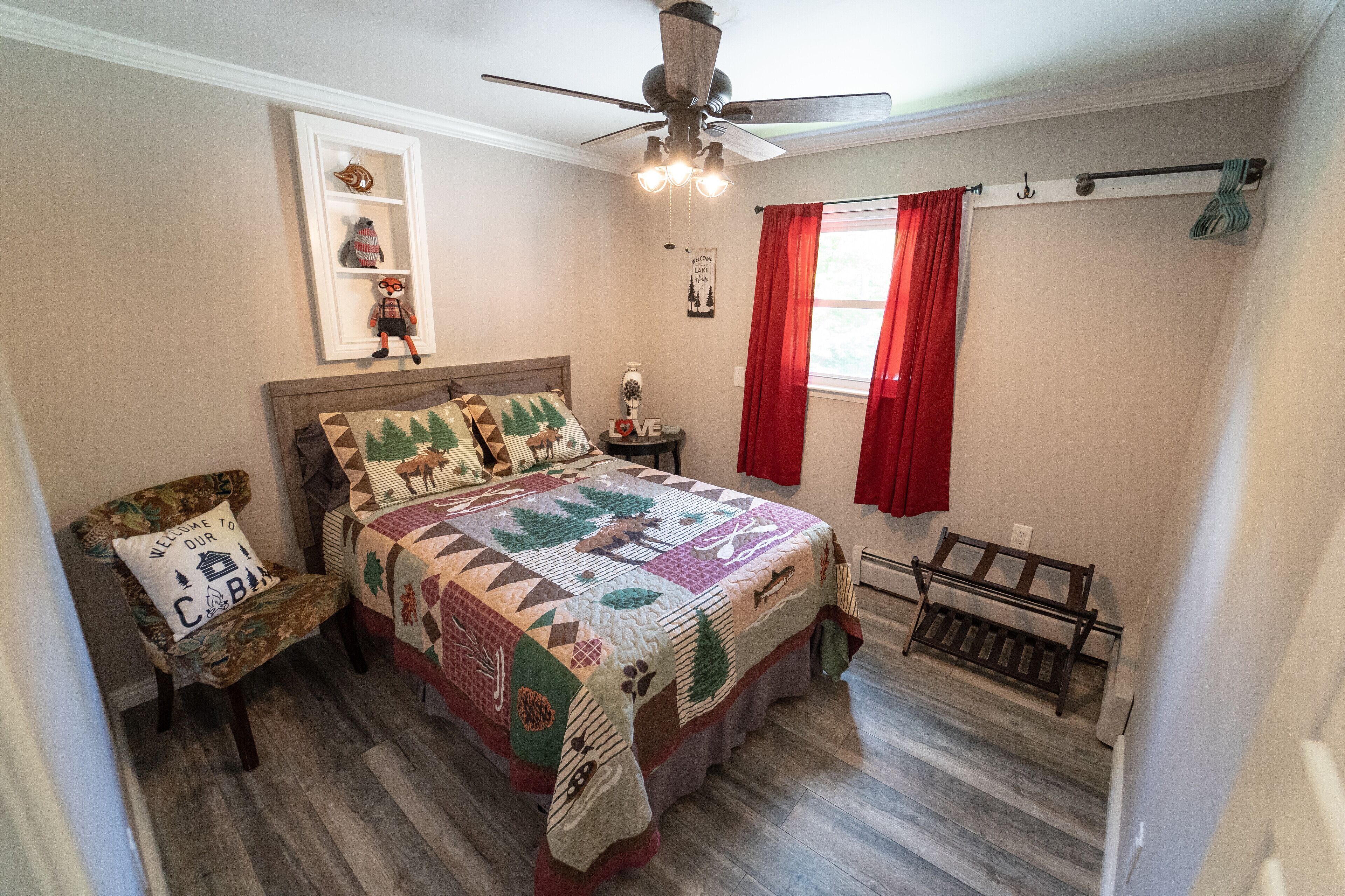 A bedroom with a bed, a chair, a nightstand, a ceiling fan, and a window with red curtains.