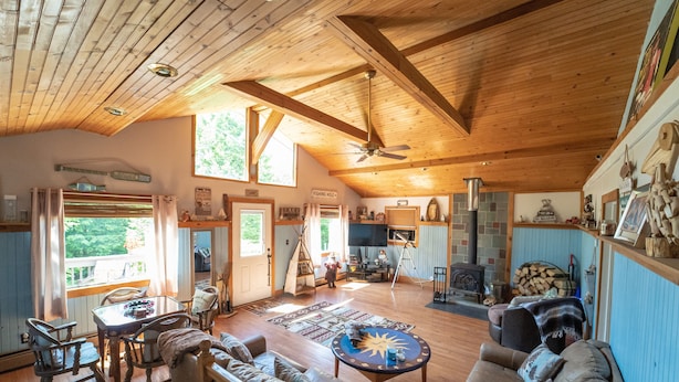 Ein geräumiges Wohnzimmer mit hohen Decken, Holzbalken, einem Kamin, einem Fernseher und einer gemütlichen Sitzecke.