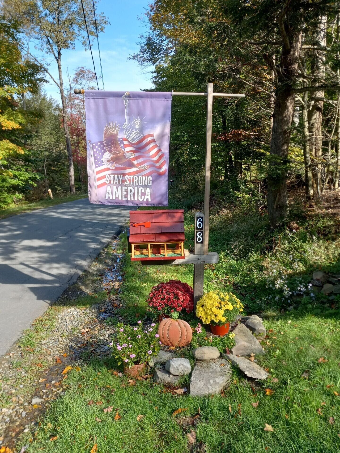 Ein Straßenschild mit einer Plakette mit der Aufschrift "STAY STRONG AMERICA" und einem kleinen rotem Hausmodell.