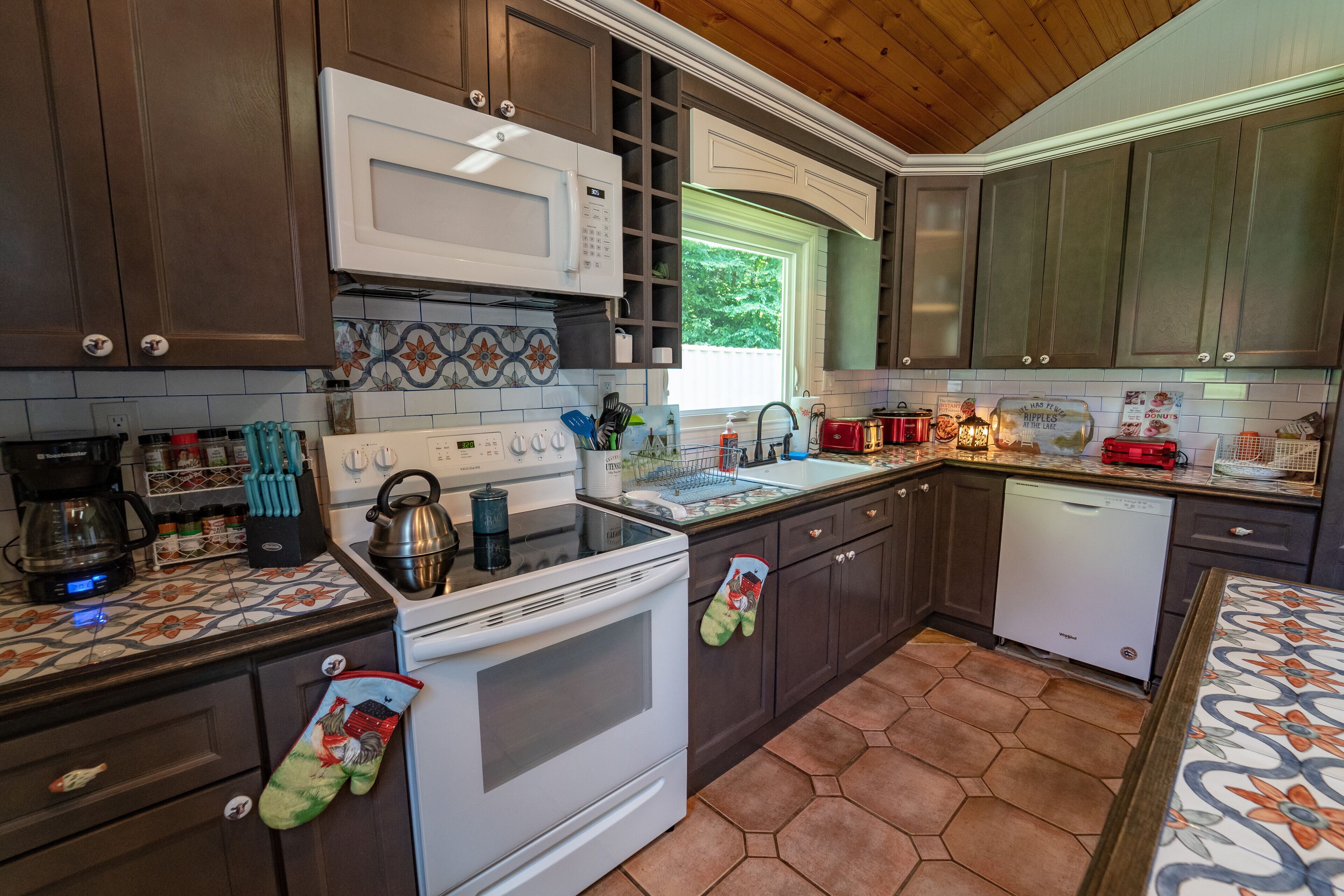 A kitchen with dark wooden cabinets, a white microwave, a stove, and a dishwasher.