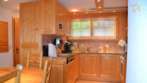A kitchen with wooden cabinets, a dining table, and a window with lace curtains. - Outside : flat for 6 persons ground floor, 40sqm south-facing balcony -Inside : about 77 sqm, open k (St-Luc)