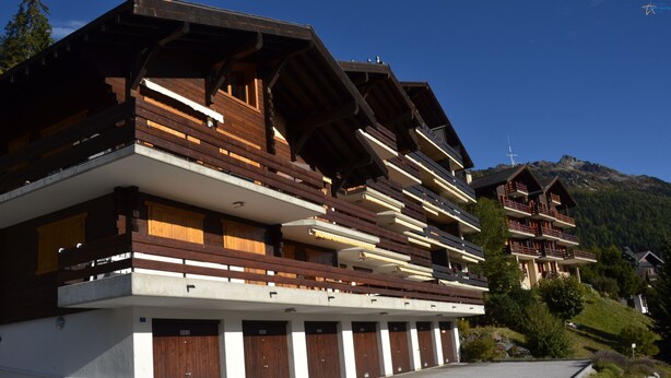 A multi-story hotel with wooden balconies, a ski lift in the background, and a mountainous landscape. - Outside : flat for 6 persons ground floor, 40sqm south-facing balcony -Inside : about 77 sqm, open k (St-Luc)