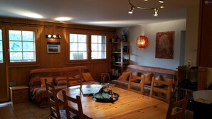 A cozy cabin interior with a wooden dining table, chairs, a sofa, and a bookshelf. - Outside : flat for 6 persons ground floor, 40sqm south-facing balcony -Inside : about 77 sqm, open k (St-Luc)