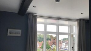 A bedroom with a large window, a bed, and a view of a river and buildings. - The Courtyard (Bewdley)